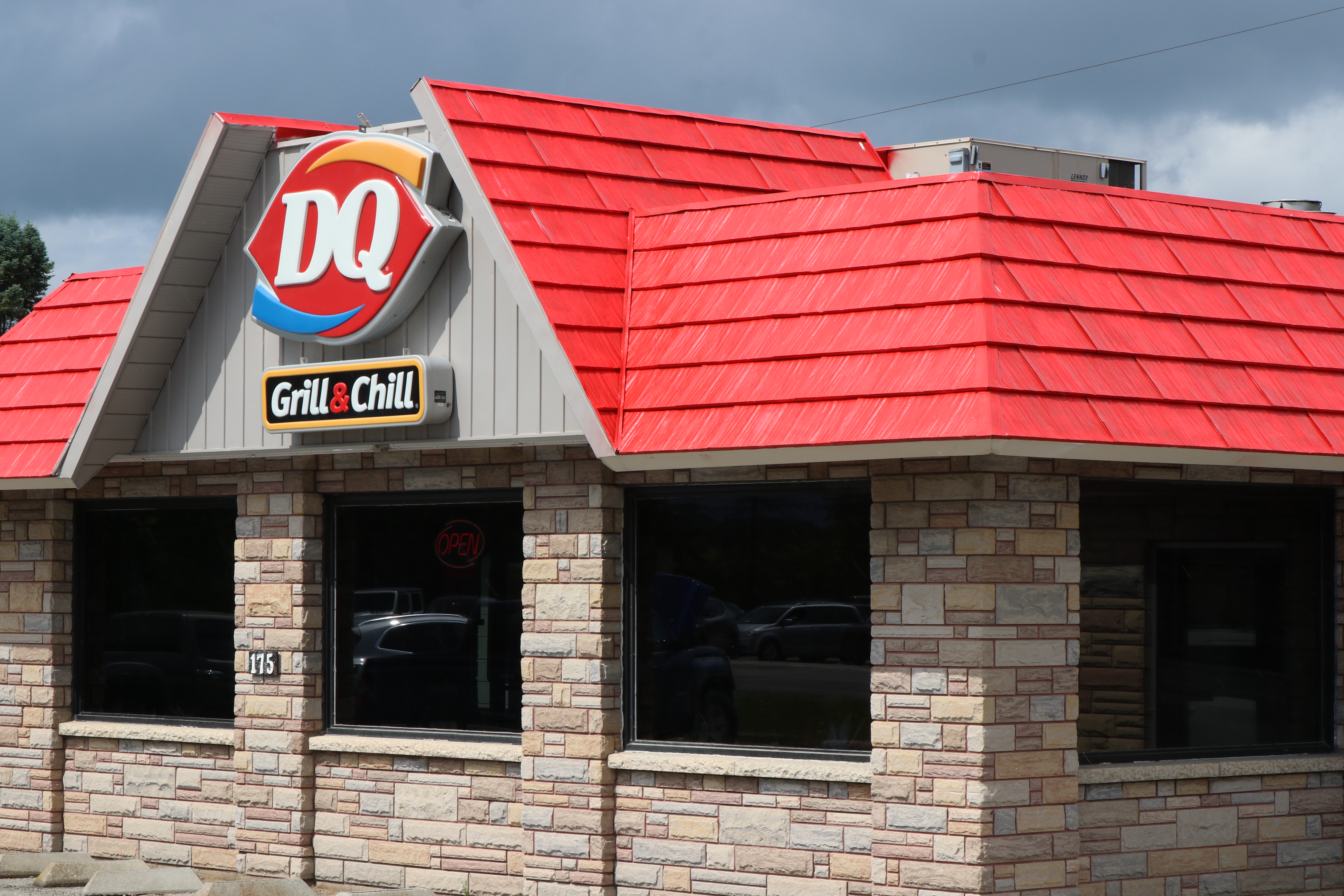  A Dairy Queen restaurant with a red-roofed brick and stone exterior, featuring a sign for a chain offering burgers, fries, shakes, and ice cream, with a drive-thru, under a cloudy daytime sky and parking lot.
