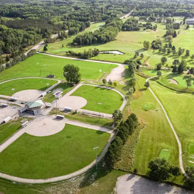 Aerial view of a ball diamond complex next to a golf course surrounded by greenery