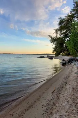 A sandy beach with calm water and scattered rocks, with the sky glowing in shades of blue and orange at sunset