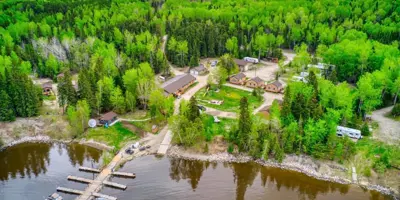 Aerial view of a fishing lodge, cabins, and boat docks surrounded by lush green forest